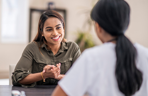 A stressed-out woman is chatting with her mental health counselor. She is explaining her problems. She is staying positive with a smile.