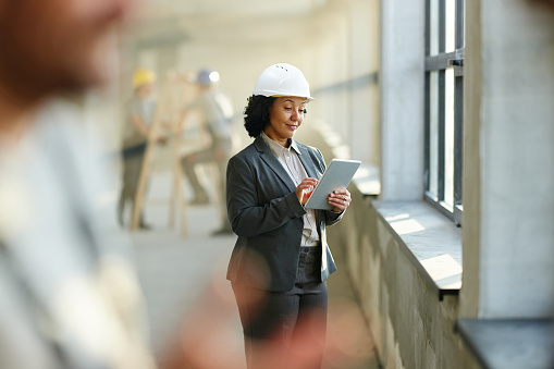Smiling female real estate developer surfing the Internet on digital tablet at construction site.