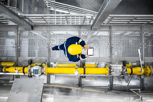 Top view of refinery worker walking by gas pipes, checking gasoline supply and installations in production plant.