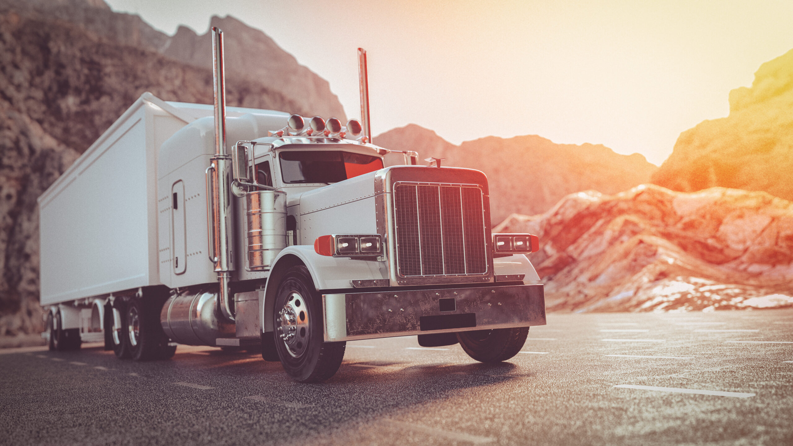 A semi truck driving along a winding road surrounded by majestic mountains under a clear blue sky.