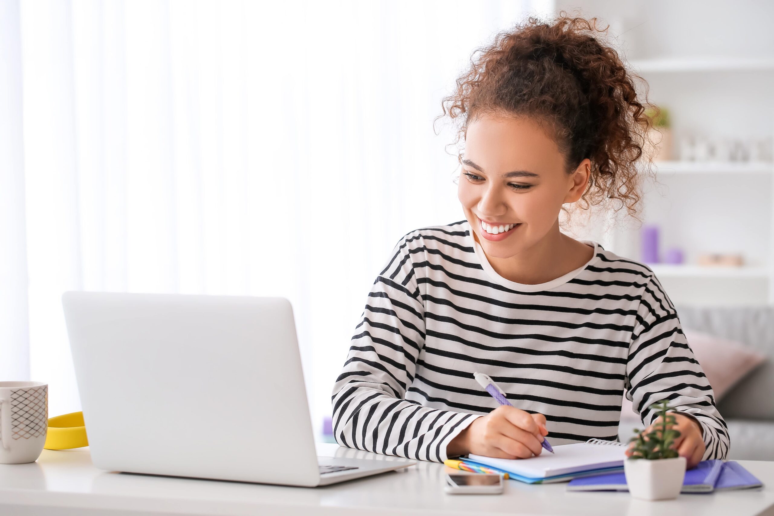 A woman smiles while focused on her laptop, showcasing a positive work environment.